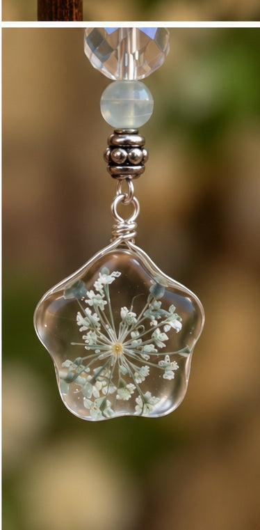 Close-up of a clear flower-shaped earring pendant with delicate white floral details and pale blue bead accents