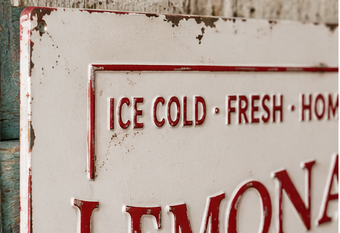 Close-up of raised red Ice Cold Fresh Homemade lettering and distressed finish on the Lemonade metal sign