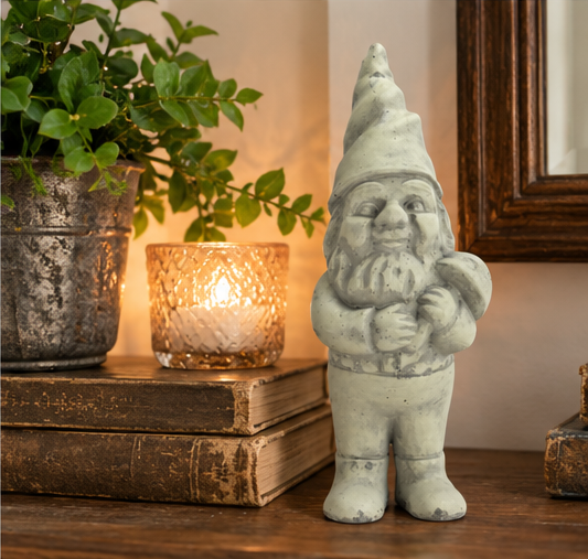 Clifford cement garden gnome displayed on a wooden tabletop beside vintage books, greenery, and candlelight