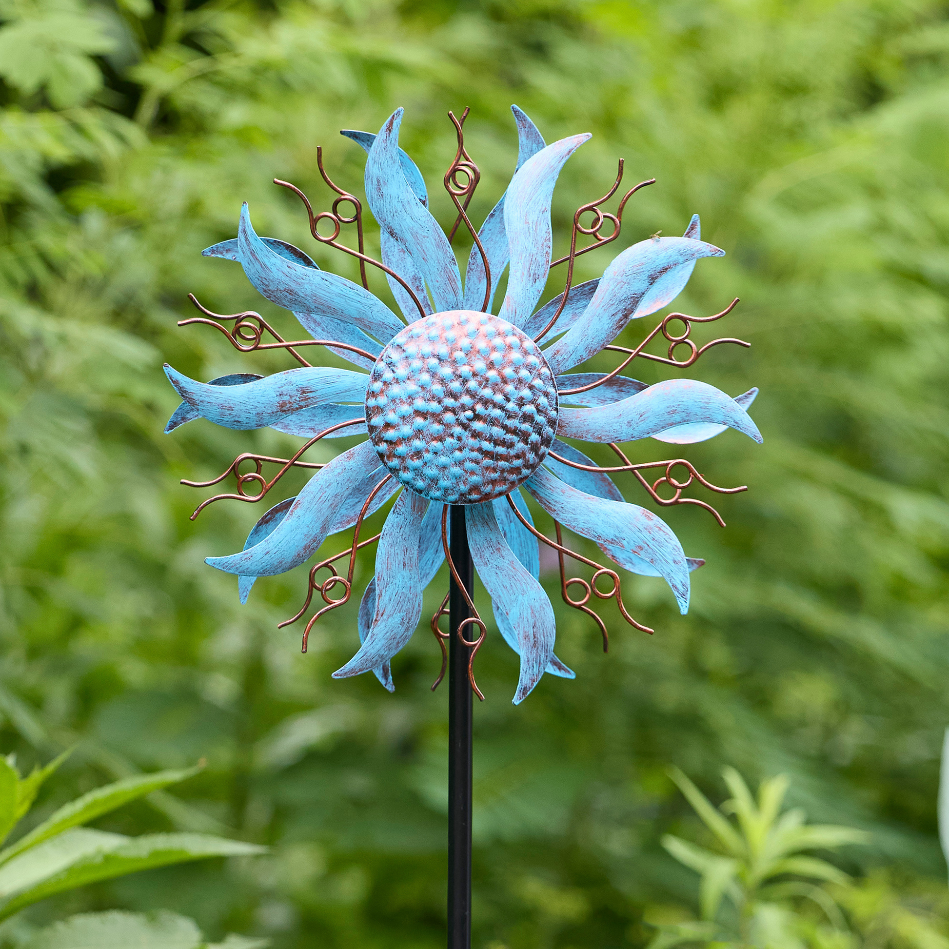 Full-length view of blue and bronze coneflower wind spinner on black steel pole stake in garden