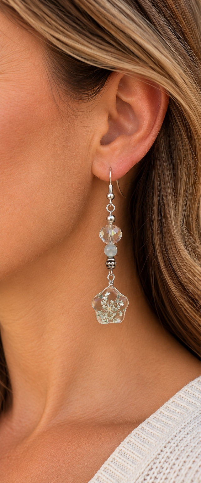 Woman wearing a white floral dangle earring with a clear flower-shaped pendant and pale blue bead accent