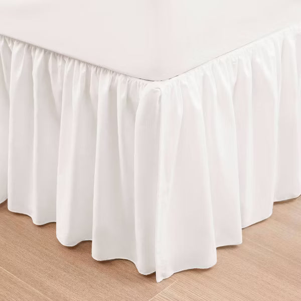 White gathered bed skirt shown around the corner of a bed.