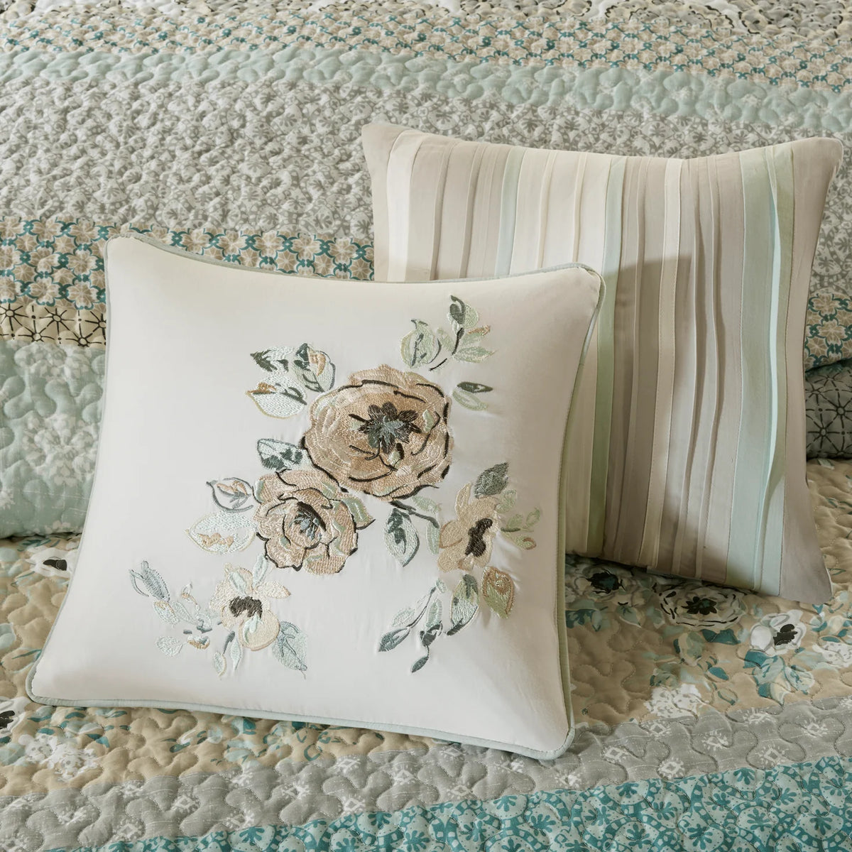 Close-up of the Madison Park set’s floral embroidered pillow and pleated cream pillow against the patterned coverlet.
