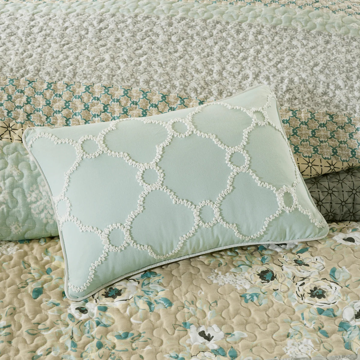 Aqua decorative pillow with raised cream geometric detailing on the Madison Park floral coverlet.
