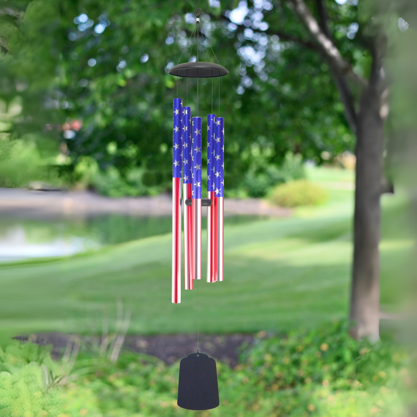 Patriotic USA American flag wind chime with 5 aluminum tubes in red, white, and blue stars and stripes, hanging outdoors in a lush green garden setting, 56 inches long