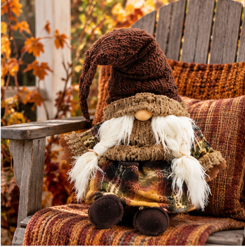 Rustic Harvest Gnome Plush with a brown knit hat and braided white beard seated on a weathered wooden chair with rust-colored autumn textiles
