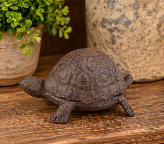 Antique brown turtle key hider displayed on a wooden shelf beside weathered planters and greenery.
