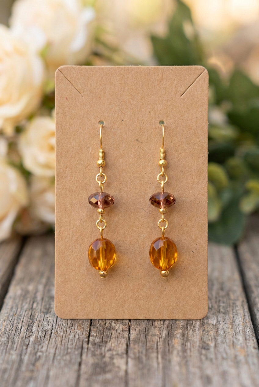 Handmade amber glass bead earrings with smoky rose-brown accent beads and gold hooks displayed on a kraft jewelry card