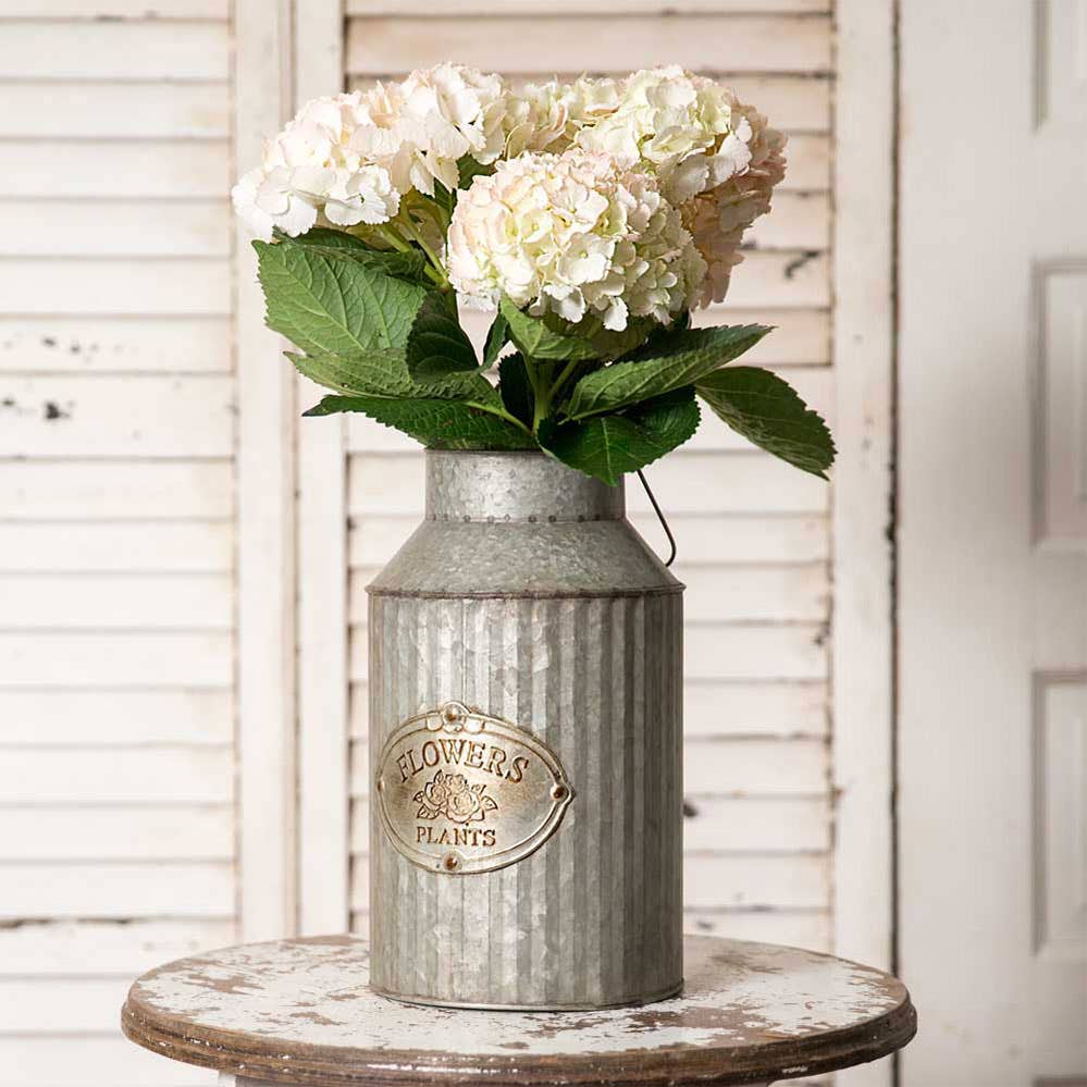 Silver-tone metal Flowers & Plants can holding white hydrangeas on a round wooden table.