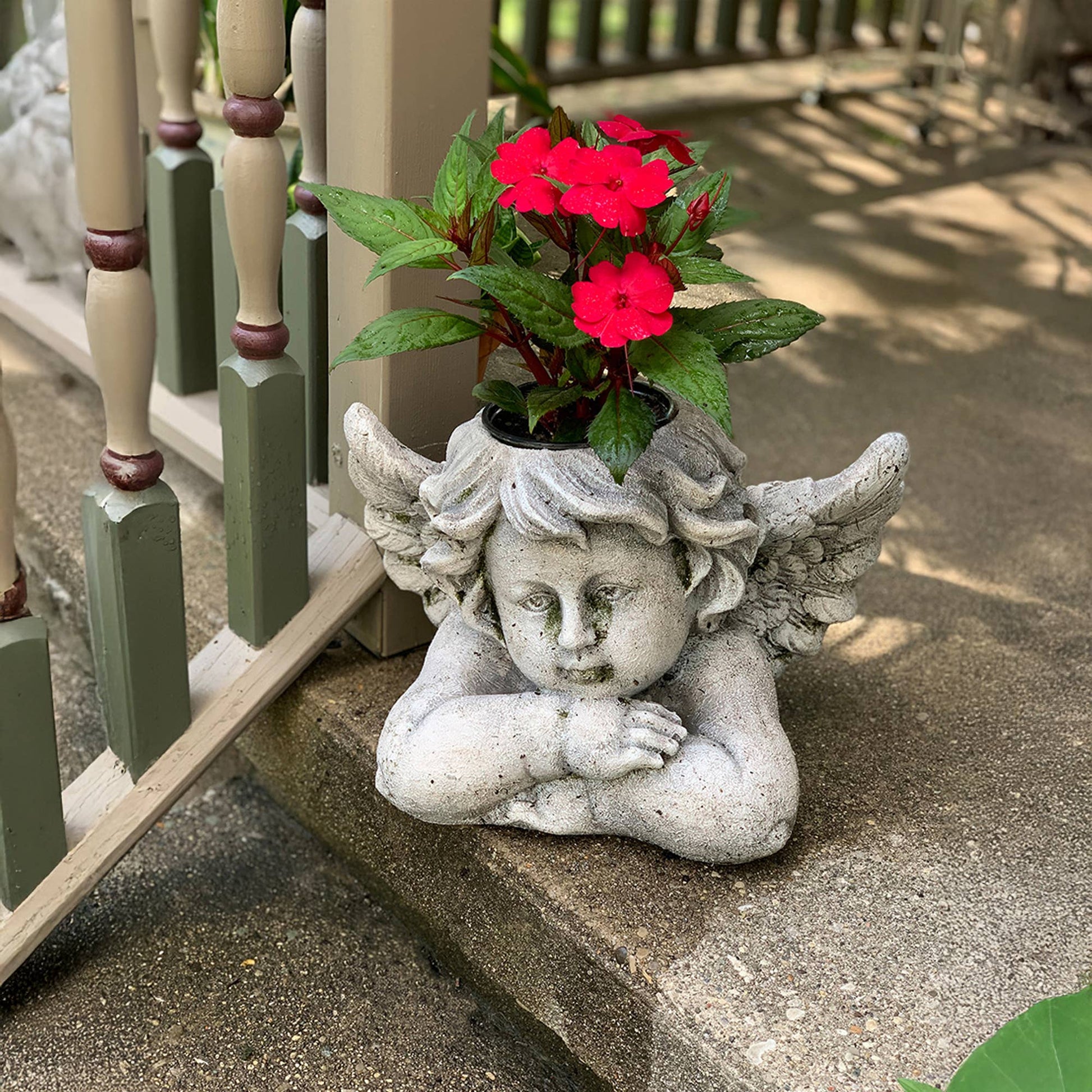 Cherub garden planter holding red impatiens on a porch step with white railing