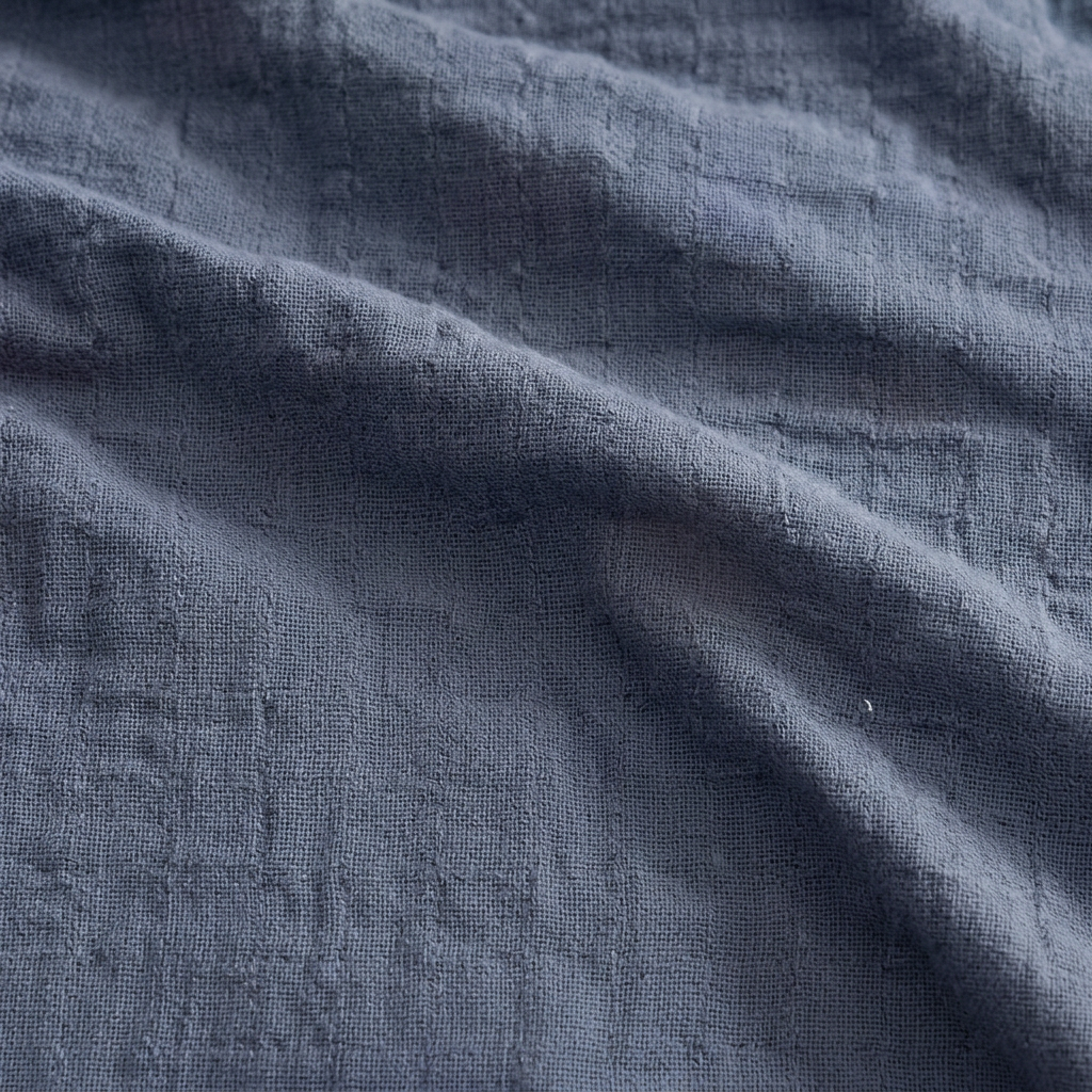 Clean Spaces denim-blue cotton gauze blanket folded on a white background.