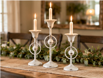 Set of three distressed white Evelyn metal taper candle holders with lit candles on a rustic dining table