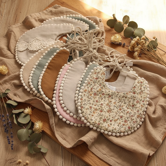 Vintage floral baby bandana bib with tassel fringe on a warm natural wood surface with dried florals and soft linen