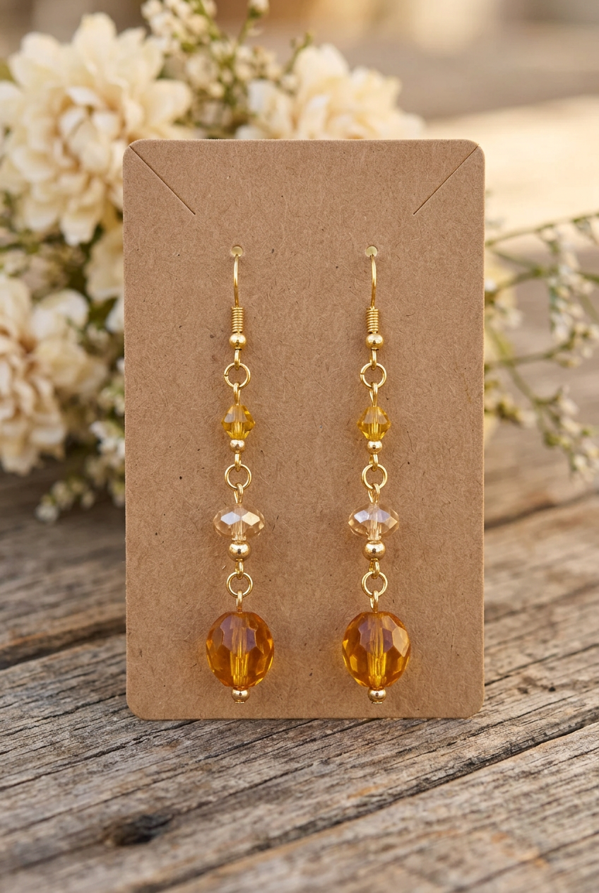 Handmade amber, champagne, and golden-yellow glass bead earrings with gold double hoop links displayed on a kraft jewelry card