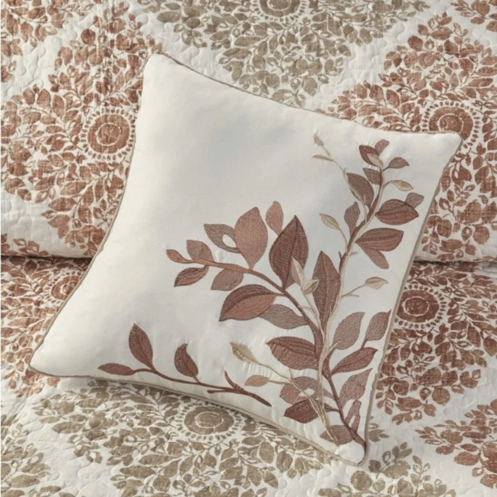 Cream decorative pillow with spice-colored embroidered leafy branches on Madison Park Claire patterned bedding.